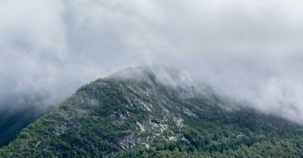 Mist-covered mountain ridge with rocky slopes and green forests at the base.