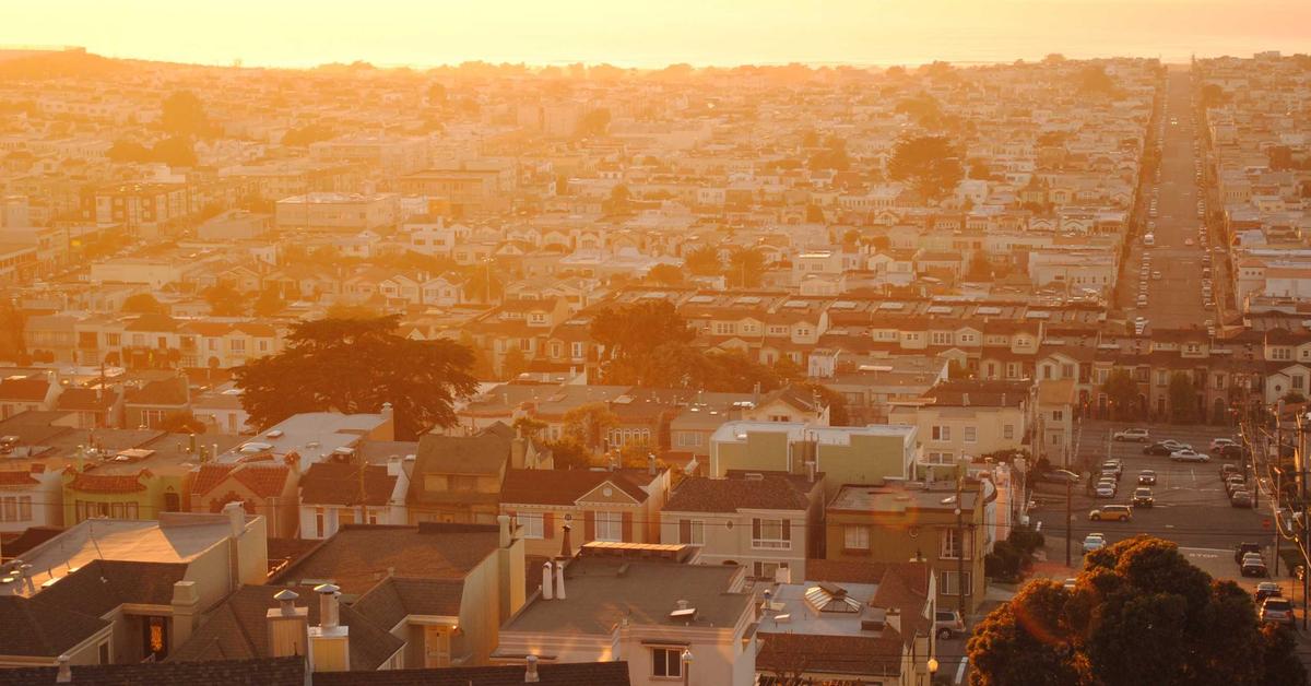 Aerial view of a dense residential neighborhood bathed in warm orange sunset light, with rows of houses stretching toward the horizon.