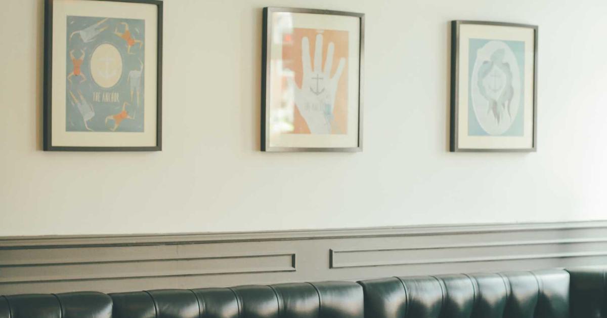 Three framed abstract posters hung in a row on a pale wall above a dark leather banquette in a seating area.