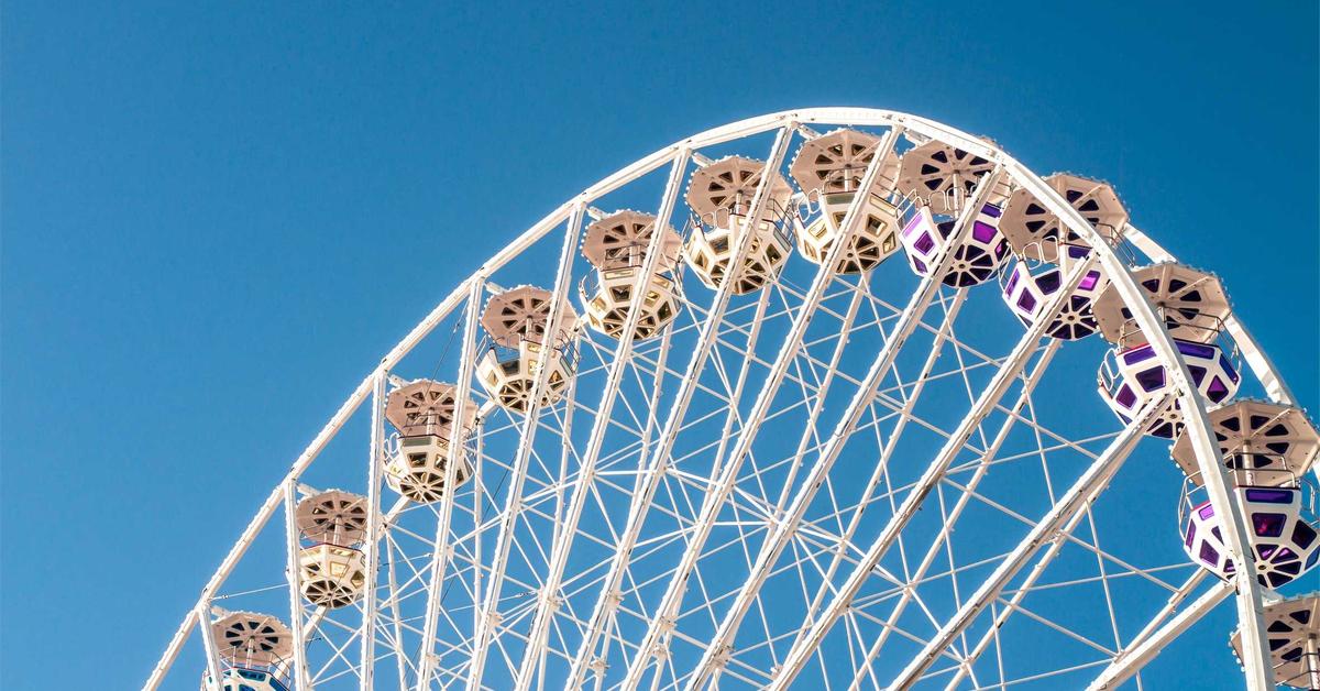 White Ferris wheel with colorful gondolas against a clear blue sky, partial view of the ride at an amusement park.