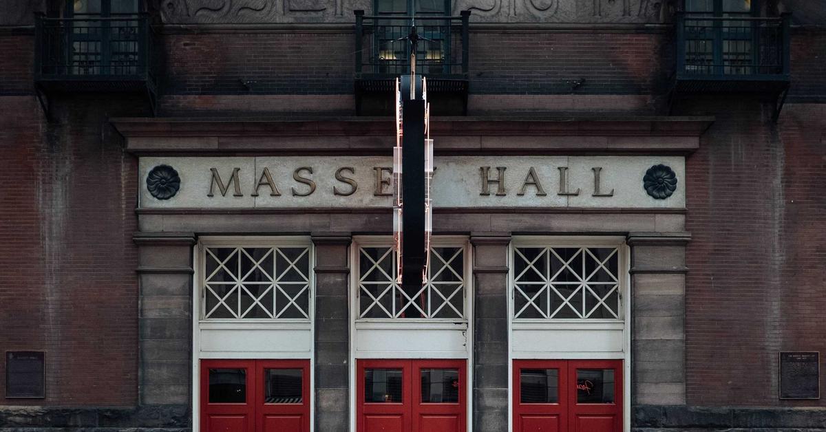 Front of Massey Hall with red doors, brick facade, and a tall dark hanging sculpture centered above.