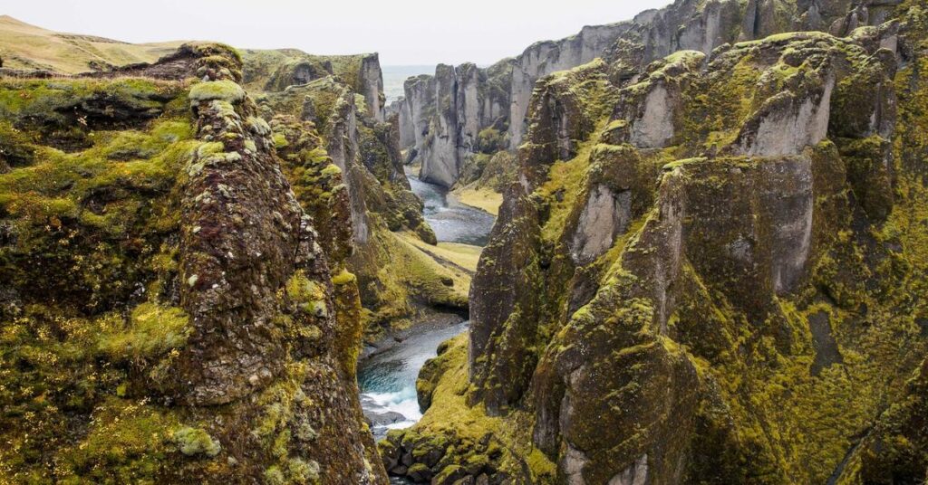 Rugged mossy canyon with steep rock walls and a winding river through the gorge.