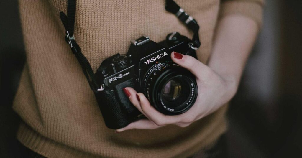 Person in a brown knit sweater cradling a black Yashica FX-3 Super camera against their chest.