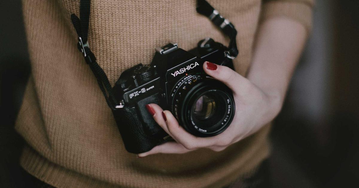 Person in a brown knit sweater cradling a black Yashica FX-3 Super camera against their chest.