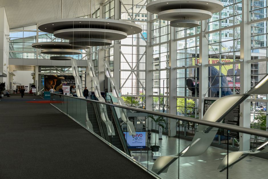 Modern convention center lobby with glass walls, circular pendant lights, and a glass-railed escalator running along the concourse.